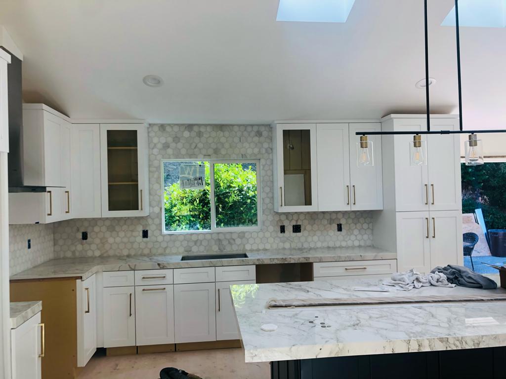 Kitchen remodel by First Choice Construction with white cabinetry, marble countertops and black pendant lighting