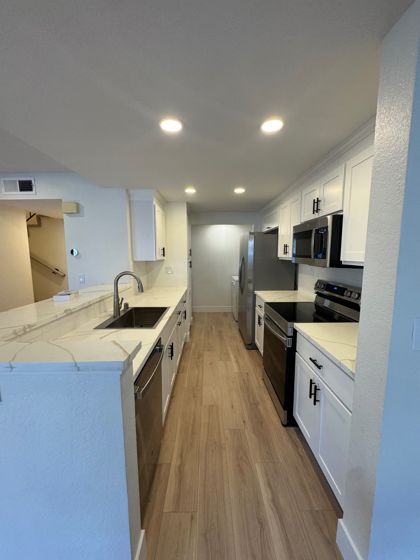 Remodeled galley kitchen with white shaker cabinets, quartz counters and wide plank flooring